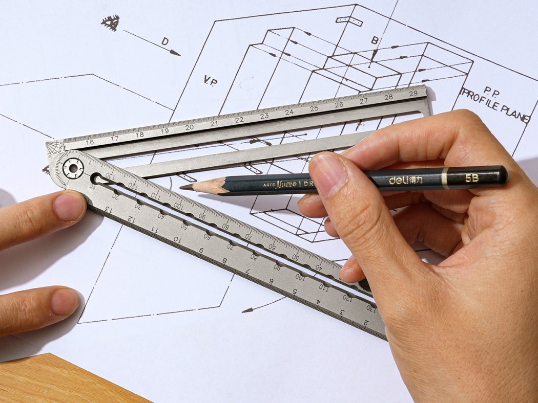 Architect's hand using a metal ruler and pencil over blueprints for drafting work on a desk
