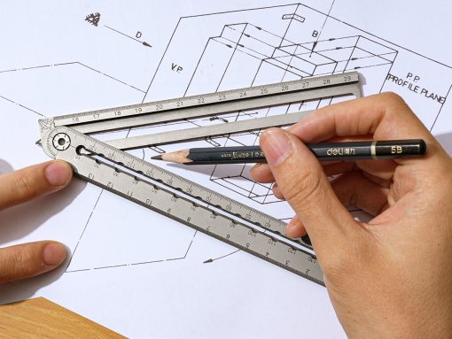 Architect's hand using a metal ruler and pencil over blueprints for drafting work on a desk