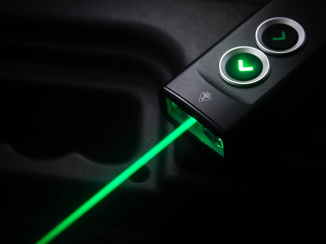 Close-up of a dark device with two circular green-lit buttons labeled L, emitting a green laser beam downward.