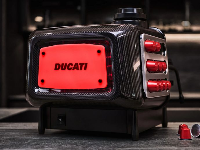 Close-up of a carbon-fiber Ducati portable power unit with a red illuminated panel reading DUCATI on a workshop surface.