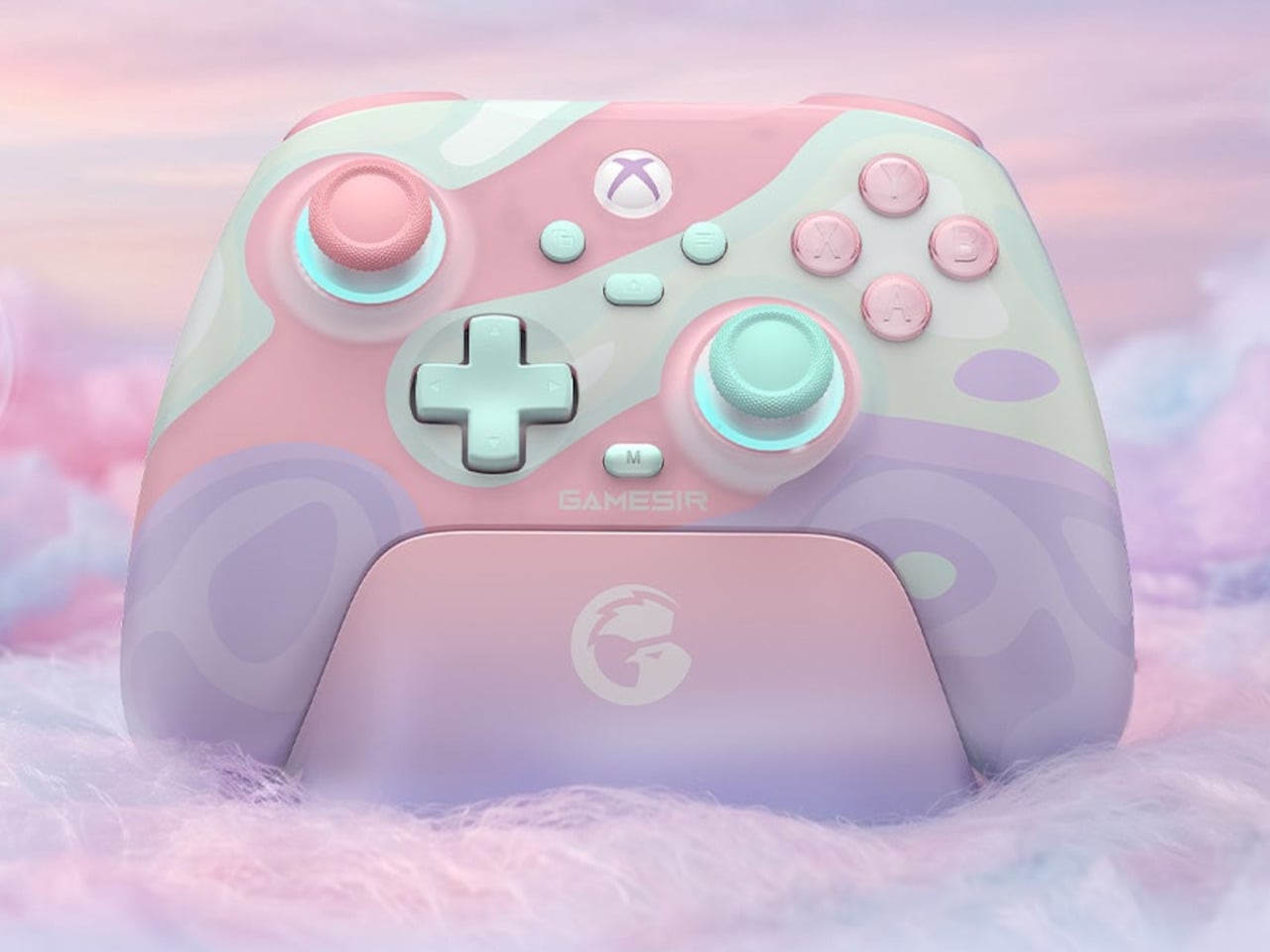 Pastel pink and mint Xbox wireless controller on a matching charging dock with a fluffy pastel backdrop.