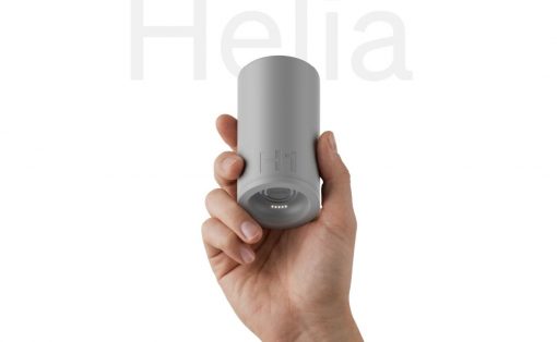Hand gripping a small gray cylindrical gadget with a glowing LED ring at the bottom, held vertically against a white background.
