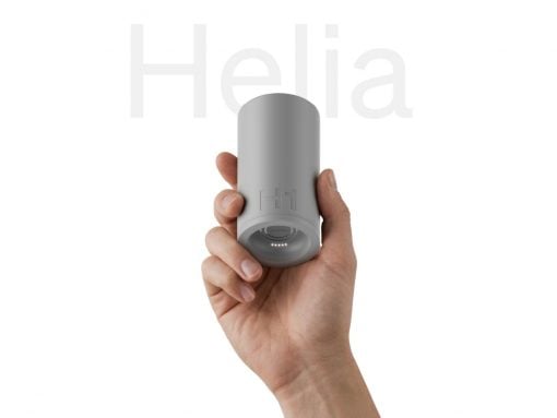 Hand gripping a small gray cylindrical gadget with a glowing LED ring at the bottom, held vertically against a white background.