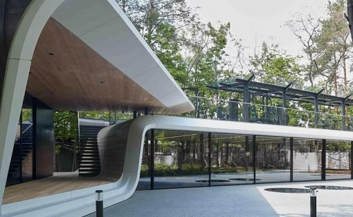 Contemporary curved white pavilion with a wooden inner ceiling and glass walls, set beside a blue-toned outdoor deck area.