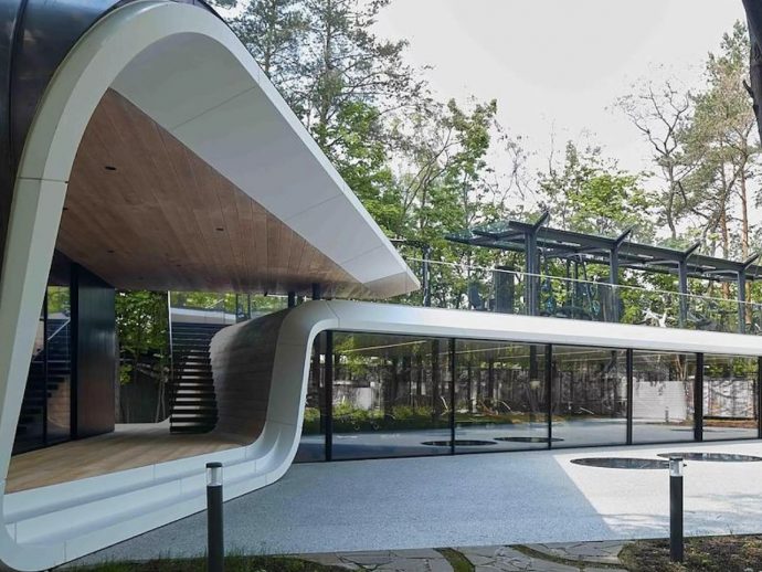 Contemporary curved white pavilion with a wooden inner ceiling and glass walls, set beside a blue-toned outdoor deck area.