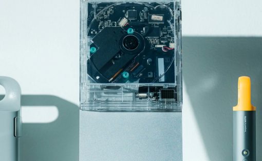 Open external hard drive enclosure revealing its internal circuit board and drive on a light desk, with a yellow-handled tool nearby.