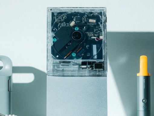Open external hard drive enclosure revealing its internal circuit board and drive on a light desk, with a yellow-handled tool nearby.