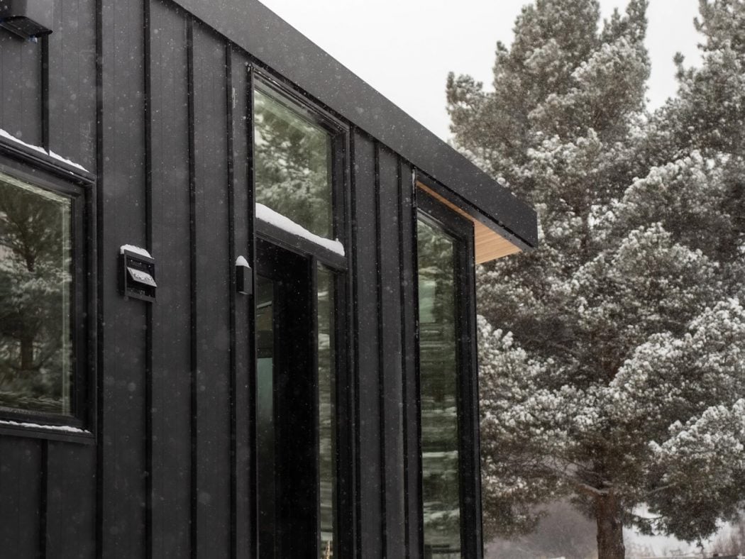 Modern black metal house exterior with large glass windows in a snowy landscape.