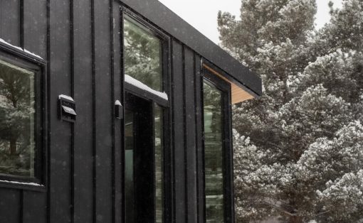 Modern black metal house exterior with large glass windows in a snowy landscape.