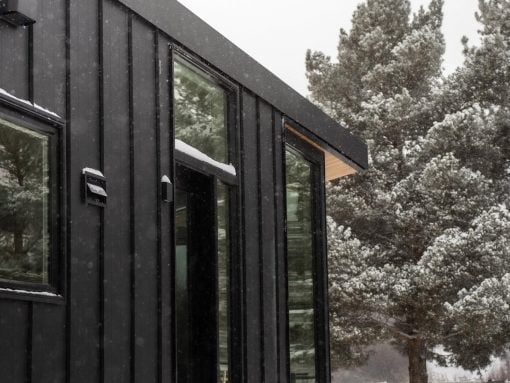 Modern black metal house exterior with large glass windows in a snowy landscape.