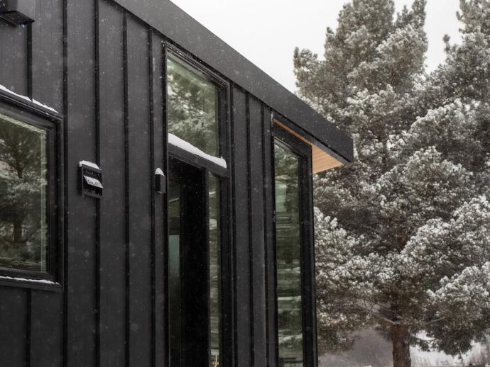 Modern black metal house exterior with large glass windows in a snowy landscape.