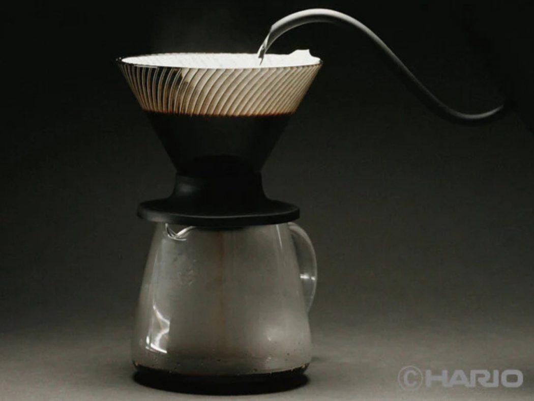 Pour-over coffee setup: a coffee filter sits atop a glass carafe against a dark background, ready for brewing on a countertop.