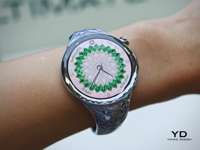 Close-up of a silver wristwatch on a bare wrist with a green geometric rosette dial and braided band.