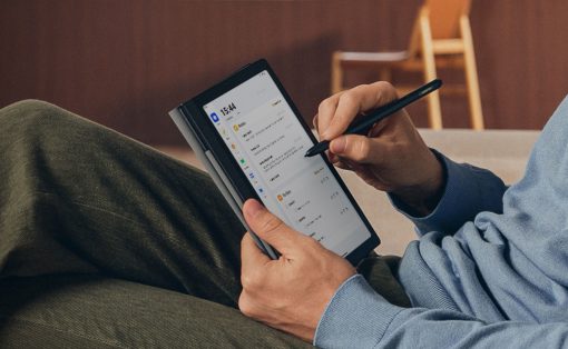 Person in a blue hoodie writes on a tablet with a stylus while reclining on green pants in a casual indoor setting.