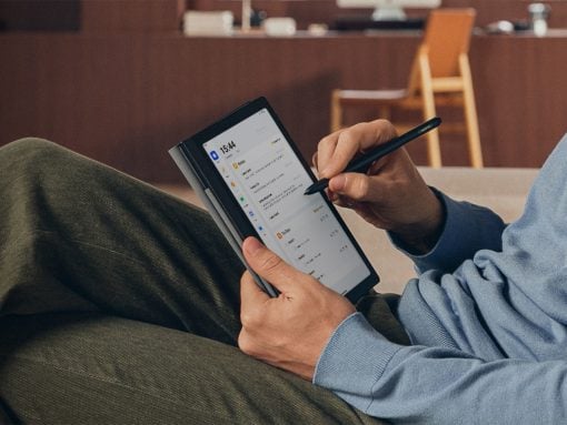 Person in a blue hoodie writes on a tablet with a stylus while reclining on green pants in a casual indoor setting.