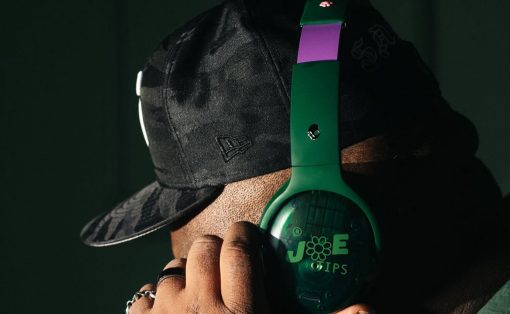 Close-up of a person wearing a black camo cap and green over-ear headphones, adjusting the headset with a hand showing rings.