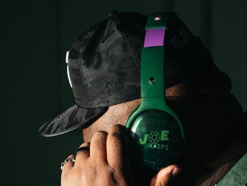 Close-up of a person wearing a black camo cap and green over-ear headphones, adjusting the headset with a hand showing rings.