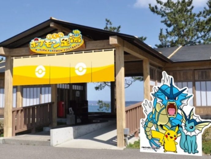 Wooden pavilion with a yellow Pokemon banner over the entrance and large Pokemon cutouts (Pikachu and blue dragon-type figures) beside it by the sea view entrance.