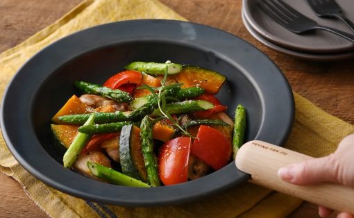 Pan with sautéed vegetables (asparagus, bell pepper, zucchini, squash) and chicken, garnished with rosemary, on a dark skillet with a wooden handle.