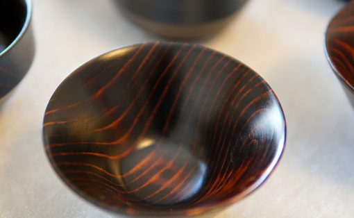 Close-up of a dark lacquered wooden bowl with reddish wood grain patterns on a light surface.