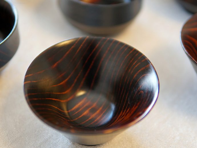 Close-up of a dark lacquered wooden bowl with reddish wood grain patterns on a light surface.
