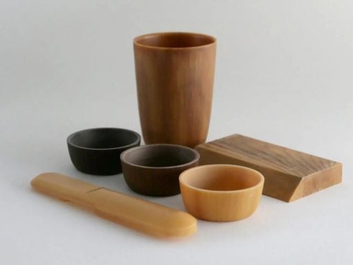 Collection of wooden kitchenware: tall cup, several bowls in black and natural wood tones, a rectangular cutting board, and a long spatula on a light surface.