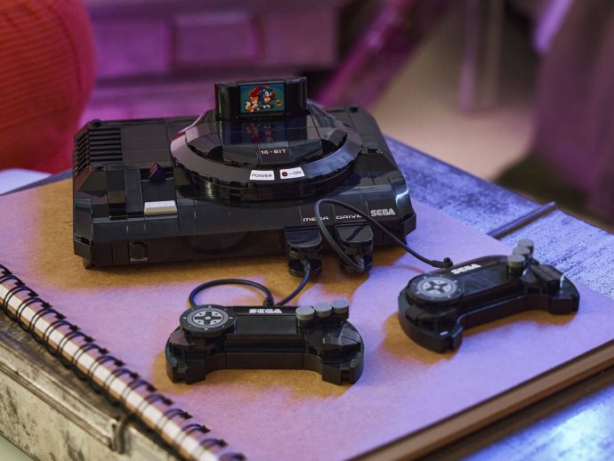 Retro Sega Mega Drive console with two wired controllers on a purple-toned notebook.