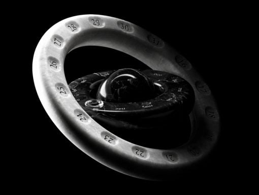 Abstract 3D sculpture: a white numbered ring looping around a glossy black inner core against a black background (artistic, geometric form).