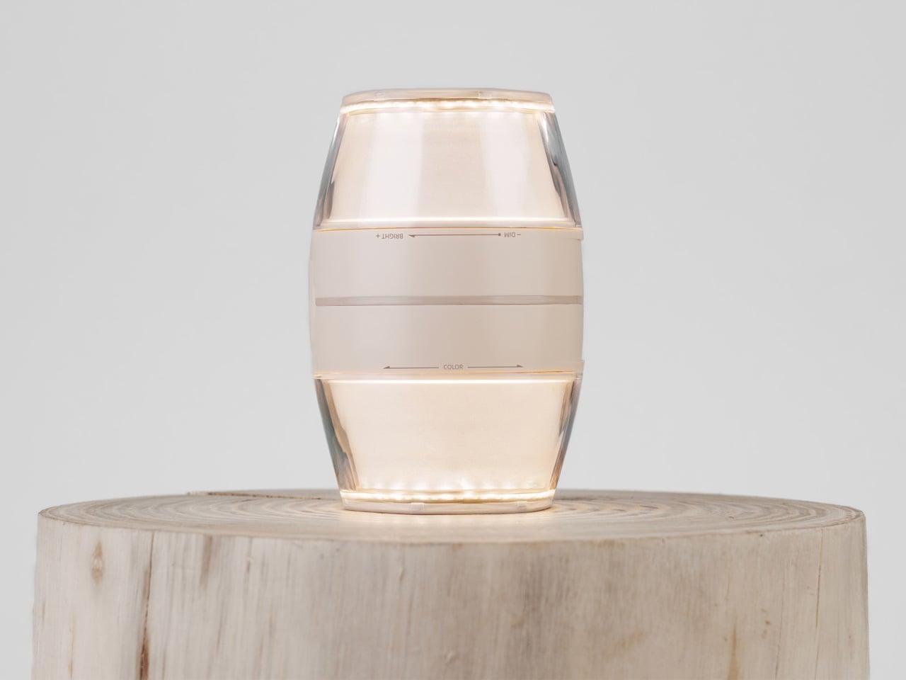 Small beige LED lamp lit with a warm glow, sitting on a round wooden stump.