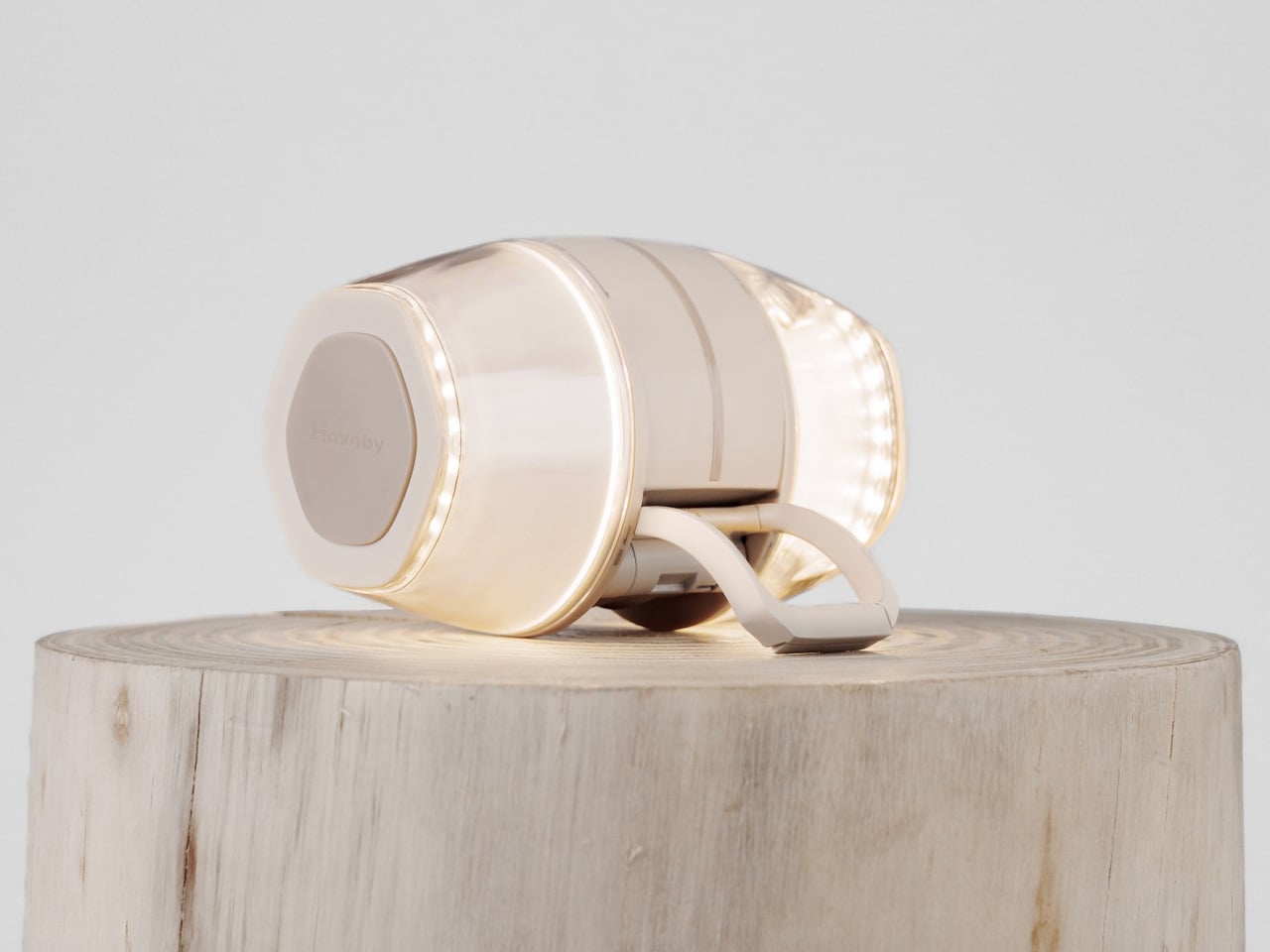 Cream wireless over-ear headphones resting on a wooden stump against a pale background.