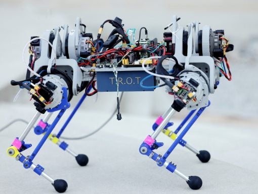 Four‑legged robot with exposed wiring and motors, walking on concrete surface; appears to be a prototype with a blue chassis labeled 'TROT'.