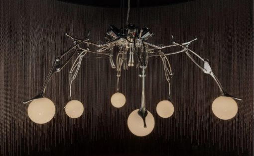 Contemporary metal chandelier with multiple curved arms and glowing glass bulbs in a dark room.