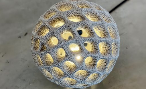 Decorative spherical lamp with a honeycomb of circular holes, warm light glowing from inside.