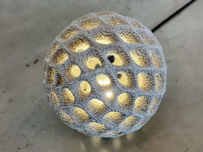 Decorative spherical lamp with a honeycomb of circular holes, warm light glowing from inside.