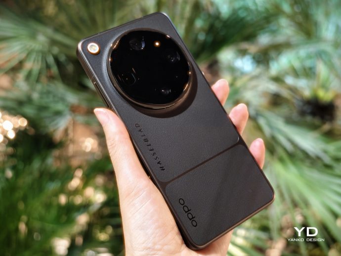Back of a black Oppo smartphone with a large circular camera module labeled Hasselblad, held in a hand outdoors.