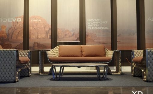 Modern lounge area with tufted beige couches and a low glass-top coffee table, showroom setting with desert backdrop mural.