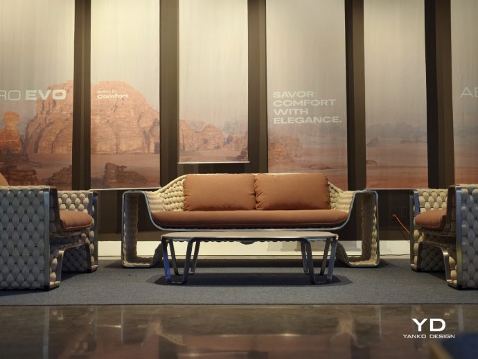 Modern lounge area with tufted beige couches and a low glass-top coffee table, showroom setting with desert backdrop mural.