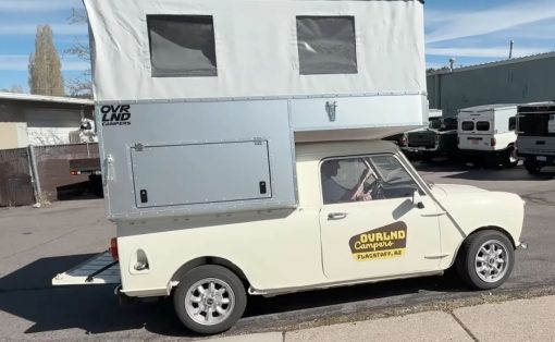 Cream vintage small van with a tall silver pop-up camper on top, parked on a street; 'Overland Campers' logo on the side and 'Flagstaff, AZ' decal on the door window.