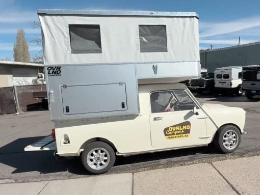 Cream vintage small van with a tall silver pop-up camper on top, parked on a street; 'Overland Campers' logo on the side and 'Flagstaff, AZ' decal on the door window.