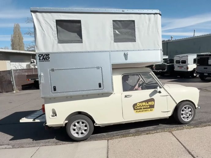 Cream vintage small van with a tall silver pop-up camper on top, parked on a street; 'Overland Campers' logo on the side and 'Flagstaff, AZ' decal on the door window.