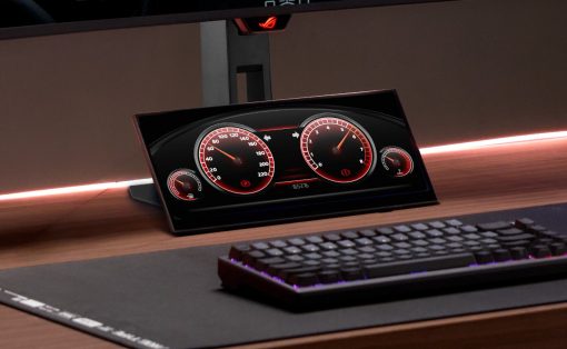 Angled monitor displaying a red-dial car dashboard on a desk, with a black keyboard and large mouse pad nearby.