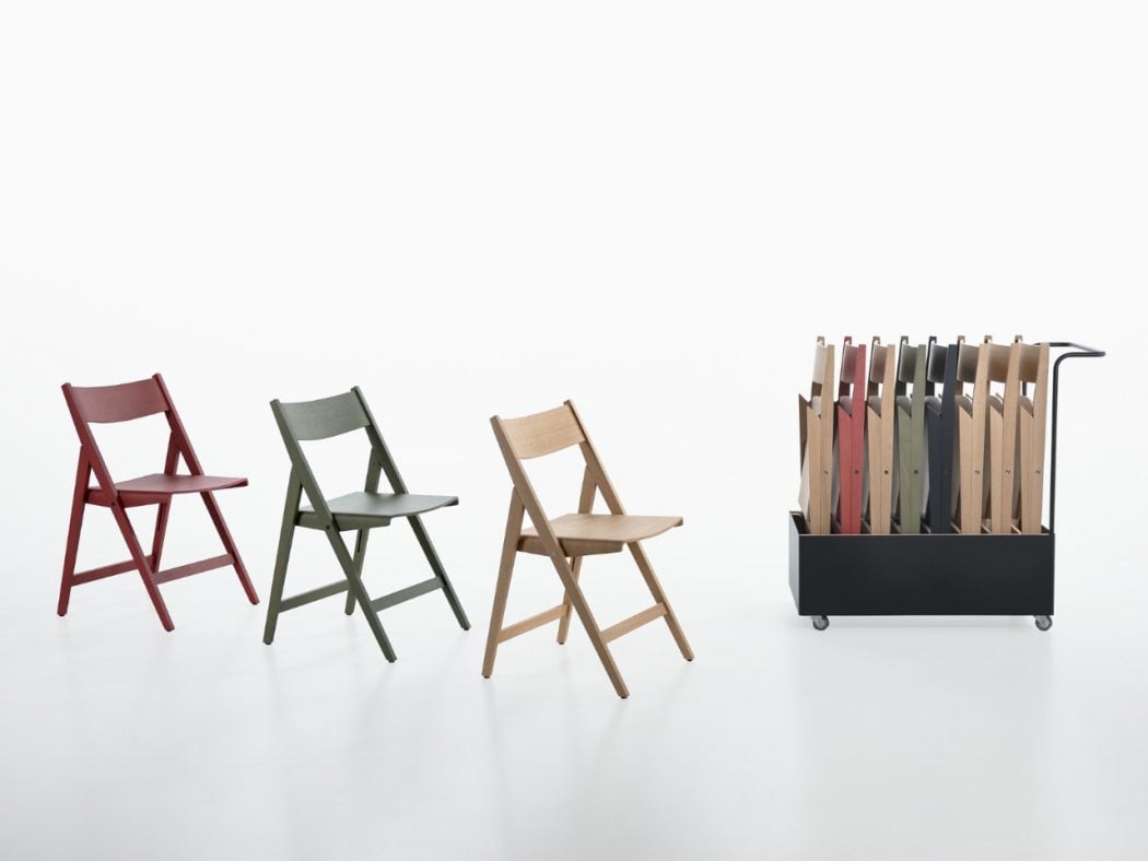 Three folding chairs in red, gray-green, and natural wood tones arranged left to center, with a wheeled black rack of color samples on the right