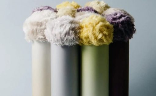 Row of pastel-colored cylinders with fluffy yarn pom-poms arranged on top, forming a soft still life.