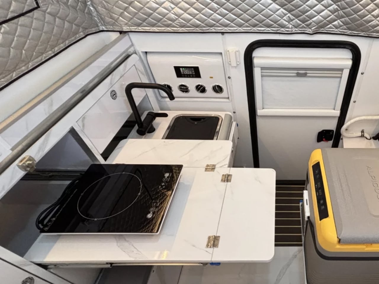 Aircraft galley with a small induction cooktop, sink, and pull-out counter for food prep and meals.