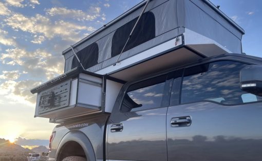 Silver pickup truck with a mounted rooftop tent in a desert at sunset, blue sky.