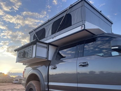 Silver pickup truck with a mounted rooftop tent in a desert at sunset, blue sky.