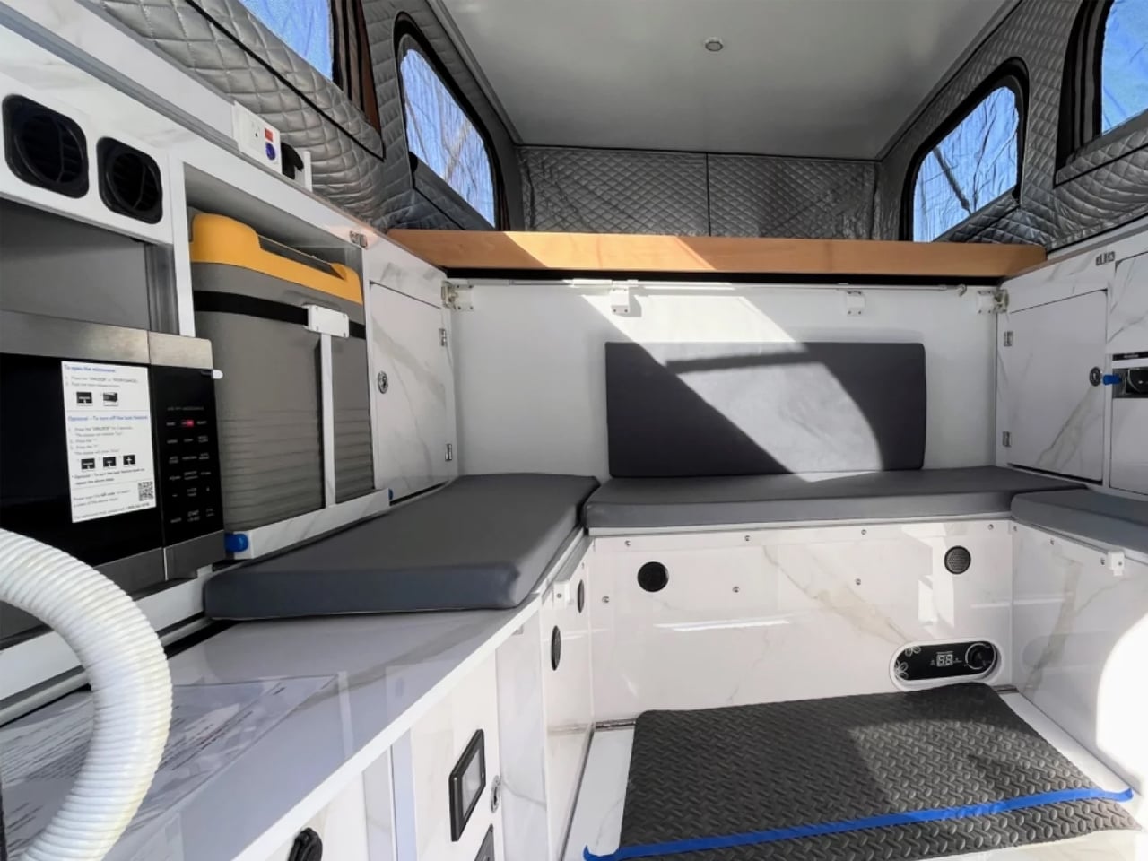 Interior of a modern ambulance with white cabinets, gray cushions, quilted walls, and a black textured floor