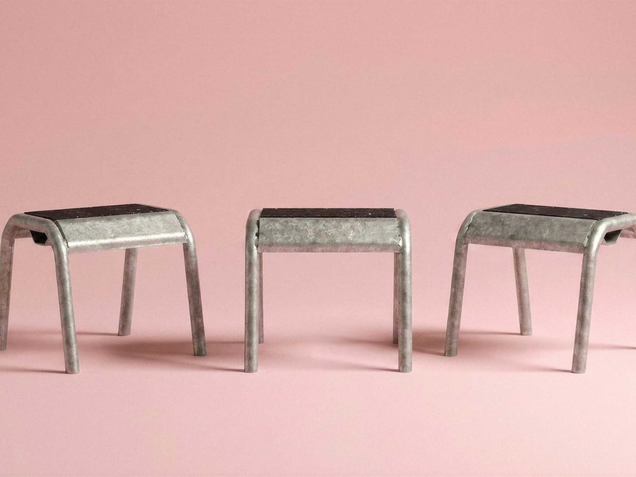 Three metal stools with black seats lined up on a pink background.