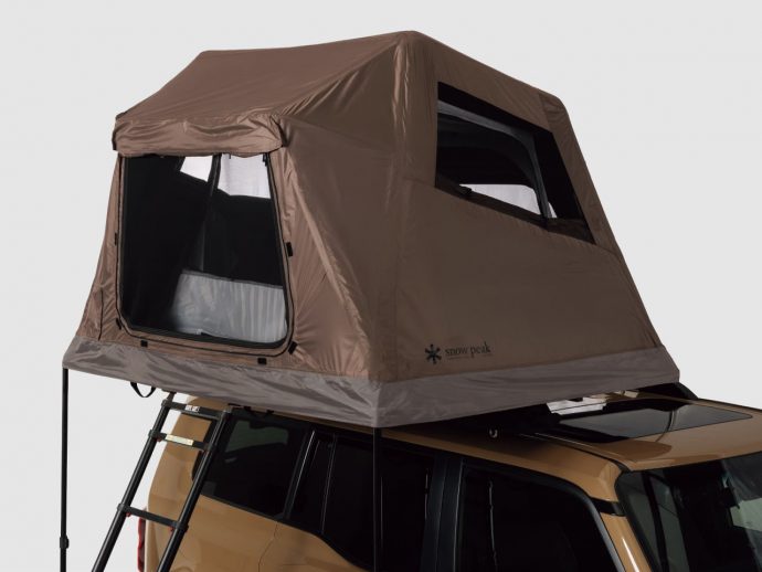 Brown rooftop tent mounted on a gold SUV with a folding ladder extending to the ground, side entry open.