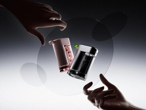 Two hands reach toward mid-air glass vials and a black-and-pink bottle, suspended inside translucent rings against a gray gradient background.